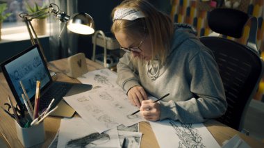 Kadın animasyoncu, çizgi film için çizimler yapar. Önündeki dizüstü bilgisayara bakar ve kağıda çizer. Çizgi Roman Derlemesi. Ön yapım için Storyboard film düzeni.