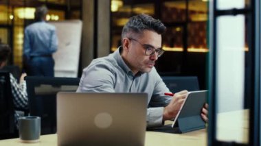 Tablet bilgisayar ve dijital kalem kullanan erkek ofis çalışanı, modern ofiste başlangıç projesi, iş stratejisi veya web sitesi tasarımı üzerinde çalışıyor. IT şirketinde çalışıyorum.