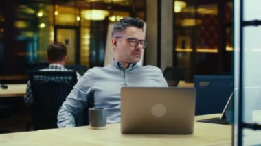Müzik dinleyen yaratıcı bir erkek ofis çalışanı, dizüstü bilgisayar ve dijital tablet bilgisayar kullanıyor, yeni başlayan projelerde iş arkadaşlarının yanında modern ofiste çalışıyor. Şirketin iş stratejisi üzerinde çalış