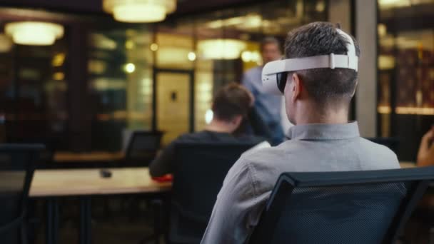 穿着Vr耳机 使用无线控制器 在虚拟现实中观看数据的人的背景图 与不同的同事在高科技公司的现代办公室工作 网络空间数字技术 — 图库视频影像