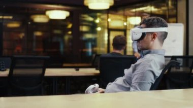 VR kulaklık takan, kablosuz kumanda kullanan ve sanal gerçeklikte veri izleyen bir adamın arka planı. Çeşitli iş arkadaşlarıyla yüksek teknoloji şirketinin modern ofisinde çalışmak. Siber uzay dijital teknolojisi