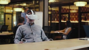 VR kulaklık ve kablosuz kontrolör kullanan, müşteriyle online konuşan, video görüşmesi yapan, yüksek teknoloji şirketinin modern ofisinde çalışan bir adam. İş sanal toplantısı. Siber uzay dijital teknolojisi