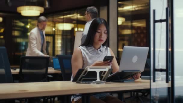 Азиатка Разговаривает Клиентом Телефону Время Работы Современном Офисе Помощью Ноутбука — стоковое видео