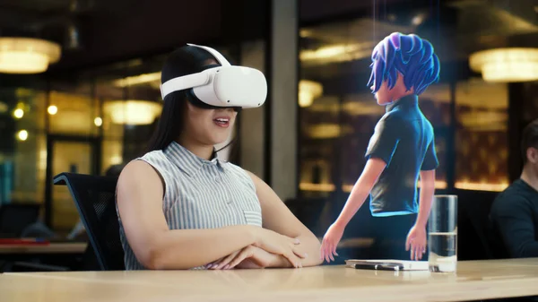 Young asian woman wearing VR headset conversing with a cartoon character avatar via an futuristic screen hologram. Futuristic communication scifi concept. 3D rendering picture. Augmented reality.