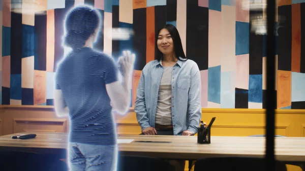 Asian woman talks on the call with her friend using augmented reality software. Hologram of her friend appears infront of her receiving the call. VFX special effects. Futuristic technology concept.