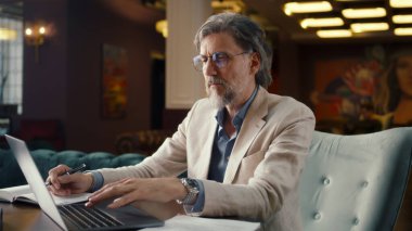 Olgun iş adamı dizüstü bilgisayarı kullanıyor, başlangıç projesi, iş stratejisi, ofis kafesinde evrak ve belgeleri analiz ediyor. E-ticaret pazarlama şirketi çalışanı.