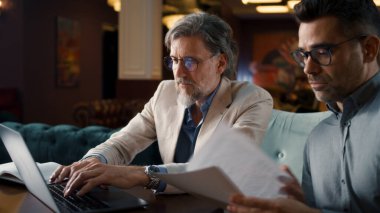 Erkek iş arkadaşları konuşuyor, dizüstü bilgisayar kullanıyor, evraklarla ve belgelerle çalışıyor, ofis restoranında iş toplantısı yapıyor. E-ticaret şirketinin stratejisi üzerine takım çalışması