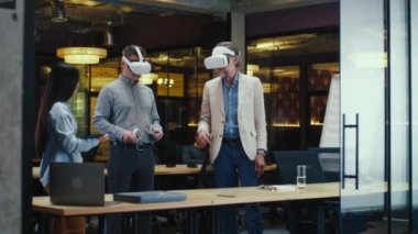 Çoklu etnik ofis çalışanları, tablet bilgisayar ve kablosuz kontrolörleri kullanarak, veri izleyerek, yüksek teknoloji şirketinin modern ofisinde çalışarak, VR kulaklıklarını birlikte test ediyorlar. Siber uzay dijital teknolojisi