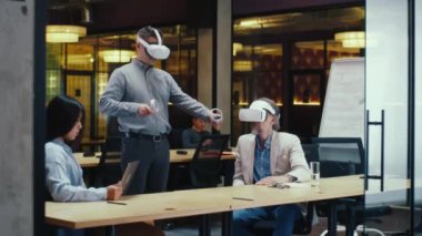 Çoklu etnik ofis çalışanları, tablet bilgisayar ve kablosuz kontrolörleri kullanarak, veri izleyerek, yüksek teknoloji şirketinin modern ofisinde çalışarak, VR kulaklıklarını birlikte test ediyorlar. Siber uzay dijital teknolojisi