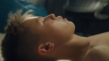 Düşünceli çocuk halılı zemine uzanmış okul spor takımıyla oynadığı futbol maçını düşünüyor. Odasında çıplak vücutlu azimli genç bir çocuk..