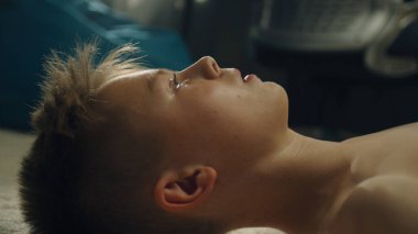 Düşünceli çocuk halılı zemine uzanmış okul spor takımıyla oynadığı futbol maçını düşünüyor. Odasında çıplak vücutlu azimli genç bir çocuk..