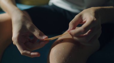 Genç bir çocuk dizine tıbbi yapıştırıcı yapıştırıyor. Yaralandıktan sonra ilk yardım. Spor yaparken kesikler, sıyrıklar ve hafif kanayan yaralar..