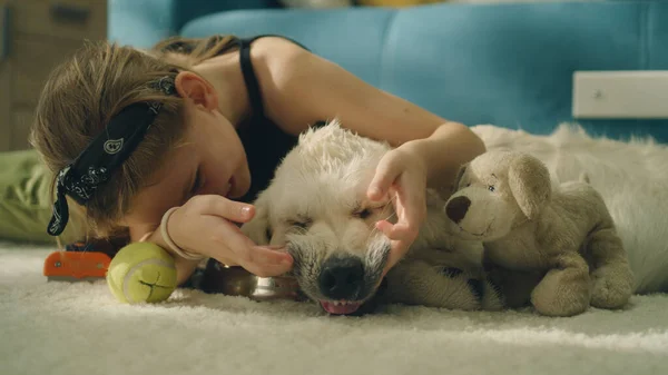 Young girl playing with dog mouth on mild carpet, watching on teeth, laughing and smiling, spending leisure time at home together with pet. Golden retriever.