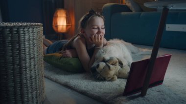 Küçük bir halıda köpekle yatan kız, evde boş zamanlarında dijital tablet bilgisayarda komik filmler izleyen, evcil hayvanlarla birlikte gülümseyen ve takılan, mutluluğu hisseden bir kız. Golden retriever.