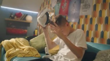 VR gözlüklü ve joystickli genç çocuk yoğun bir oyunu bitirdikten sonra koltukta oturur ve sanal gerçeklik kulaklığını çıkarır. Gelişmiş teknoloji, oyun konsepti.