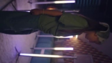 Kız kamerayı açıyor, LED lambalarla aydınlatılmış odada şarkı söylüyor ve dans ediyor, kameraya bakıyor, moda videosu yaratıyor, evde boş zaman geçiriyor. Dikey çekim. Telefon ekranı görünümü.