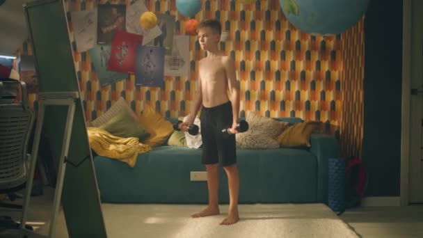 10代の少年が寝室の鏡の前でダンベルを鳴らす 上半身裸で黒のショートパンツ 学校スポーツ大会 フィットネス 体重移動の概念 — ストック動画