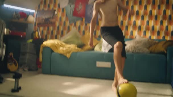 彼の寝室で試合の前に運動少年はサッカーを練習します 裸の上半身熱狂的なサッカー選手はウォーミングアップ運動を行います カーペットの上のダンベルとフォームローラー — ストック動画