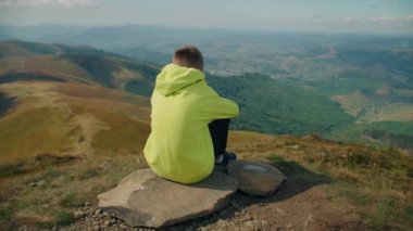 Genç adam taşın üzerinde oturuyor, güzel manzarayı seyrediyor, ılık bir rüzgar esintisi hissediyor, düşünceleri serbest bırakıyor ve boş zamanlarını dışarıda geçiriyor. Arka plan görünümü