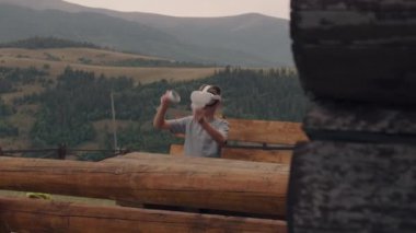 Genç adam doğada arttırılmış gerçeklik oyunları oynuyor, ahşap bankta oturuyor. Oyuncu VR gözlüklerini ve kablosuz kontrolörleri test ediyor, boş zamanlarını dışarıda geçiriyor.