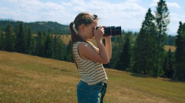 Genç fotoğrafçı doğanın resimlerini çekerek yeşil yamaçta manzara çekiyor. Portföyü inanılmaz fotoğraflarla dolduran, boş zamanlarını dışarıda geçiren bir kız. Yavaş çekim.