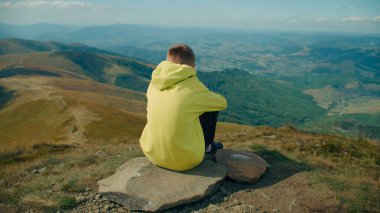 Genç adam taşın üzerinde oturuyor, güzel manzarayı seyrediyor, ılık bir rüzgar esintisi hissediyor, düşünceleri serbest bırakıyor ve boş zamanlarını dışarıda geçiriyor. Arka plan görünümü