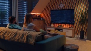 ZAPORIZHYA, UKRAINE - 13 Ekim 2022: Oturma odasındaki koltukta oturan çift, Netflix 'te TV' de korku filmi ya da aperatifler ve sodayla yayın serisi izleyen, konuşan, dinlenen ve evde dinlenen bir çift