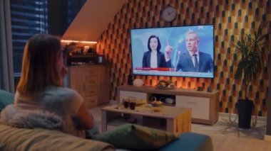 Oturma odasındaki koltukta oturan çift, Avrupa Birliği hakkında politika haberleri izliyor ve Rusya 'ya karşı yeni yaptırımlar uyguluyor. Akşamı evde birlikte geçirmek. TV canlı yayın.
