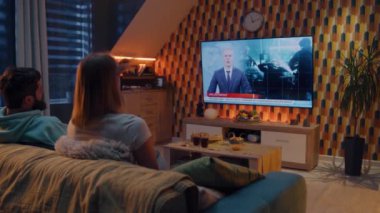 Bir çift kanepeye oturmuş abur cubur ve gazoz içiyor, konuşuyor, polis gözaltı grupları ve internet suçluları hakkında TV haberleri izliyor. Kadın ve erkek geceyi evde birlikte geçiriyorlar. TV canlı yayınları.