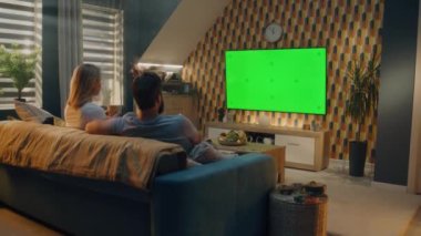 Oturma odasındaki kanepede oturan çift, son dakika haberleri, film ya da dizileri izliyor, içki ya da gazoz içiyor. Kadın ve erkek akşamları evde dinleniyorlar. Yeşil ekran. Kromakey.