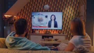 Oturma odasındaki kanepede oturup birbirlerine bakıyorlar, çocuk felci ve su kirliliği hakkında TV haberleri izliyorlar. Erkek ve kadın hafta sonunu evde birlikte geçiriyorlar. TV canlı yayın.