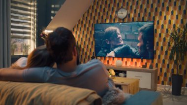 Oturma odasındaki kanepede oturan çift, TV 'de aksiyon filmi izliyor ya da canlı yayında kriminal blockbuster izliyor, konuşuyor ve oyunculuğu tartışıyor, hafta sonları evde dinleniyor. Modern dairede ev sineması.