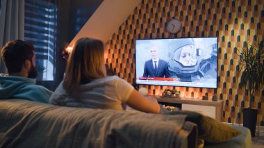 Kanepede oturan çift oturma odasında aperatiflerle, TV kanalında astronotlar, uzay görevi, Dünya yörüngesini keşfetmek hakkında haberler izliyorlar. Karı koca dinleniyor ve hafta sonları evde dinleniyor.
