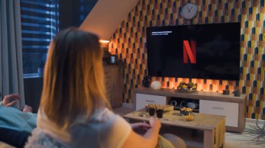 ZAPORIZHYA, UKRAINE - 13 Ekim 2022: Çift kanepede birlikte oturuyor, Netflix 'te film veya TV dizisi izliyor aperatifler, soda ve pizza ile. Kadın ve erkek evde dinleniyor..
