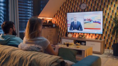 Oturma odasındaki kanepede oturan bir çift, Rus ve Birleşik Devletler arasındaki rekabetle ilgili televizyon haberleri izliyor, soğuk savaş. Kadın ve erkek geceyi evde geçiriyorlar. TV canlı yayın.