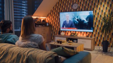 Bir çift kanepeye oturmuş abur cubur ve gazoz içiyor, konuşuyor, polis gözaltı grupları ve internet suçluları hakkında TV haberleri izliyor. Kadın ve erkek geceyi evde birlikte geçiriyorlar. TV canlı yayınları.