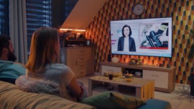 Oturma odasındaki kanepede oturan bir çift. Yanında abur cubur ve gazoz var. TV 'de felaket, terörist saldırı, bina çökmesi ve enkazdan kurtarma haberleri izliyorlar. Evde vakit geçirmek. TV canlı yayında.
