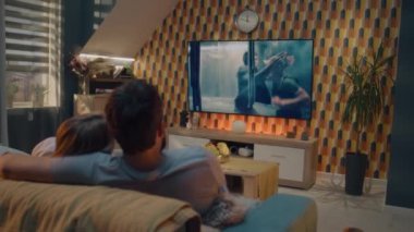 Çift rahat bir oturma odasında kanepede oturup sarılıyor, TV 'de aksiyon filmi seyrediyor ya da iş çıkışı evde dinlenen bir suçlu gişe rekortmeni. Modern dairede ev sineması.