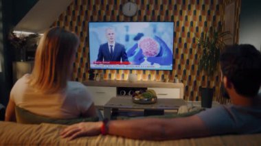 Kanepede oturan çift, yapay et, gelecekteki alternatifler ve gıda endüstrisindeki teknolojiler hakkında bilimsel TV haber kanalı izliyor. Evde birlikte vakit geçirmek. TV canlı yayın.