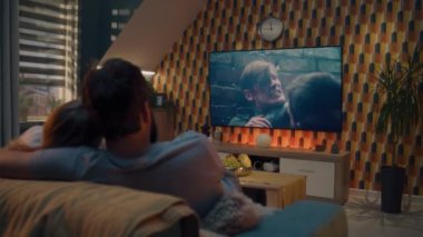 Çift rahat bir oturma odasında kanepede oturup sarılıyor, TV 'de aksiyon filmi seyrediyor ya da yayın servisinde kriminal blockbuster izliyor, hafta sonları evde dinleniyor. Modern dairede ev sineması.