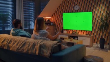 Kadın uzaktan kumandayla kanal değiştiriyor. Oturma odasında kanepede oturan, konuşan, son dakika haberlerini izleyen, TV 'de film veya dizi izleyen çift. Akşamları evde dinleniyor. Yeşil ekran. Kromakey.