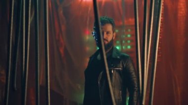 LED ışıkları olan bir kulaklık takan genç adam siyah asma çubukların arkasında durup kameraya bakıyor. Siberpunk ve fütüristik kavram. Arka planda neon ışıkları.