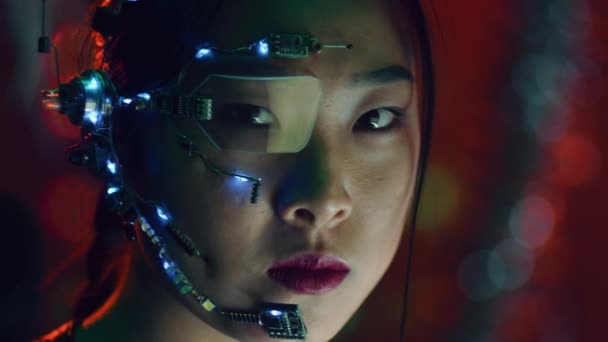 マイク ワンアイグラス ホワイトのLedライトを備えたヘッドセットを装着したサイバーパンクの女の子 背景に赤いネオンライト サイバーパンクの衣装を着たアジア系の女の子 サイバーとサイエンスの背景 — ストック動画