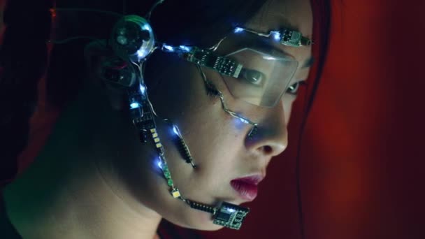 サイバーパンク衣装のアジア系の女の子がコンピュータ上で動作します 白いLedライトとマイクを備えた片目眼鏡を着用してください ネオンの背景 サイエンス フィクションサイバネティクスの概念 — ストック動画