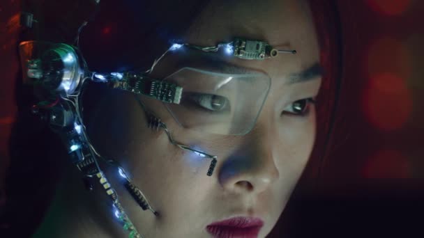 サイバーパンク衣装のアジア系の女の子がコンピュータ上で動作します 白いLedライトとマイクを備えた片目眼鏡を着用してください ネオンの背景 サイエンス フィクションサイバネティクスの概念 — ストック動画