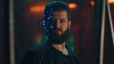 Siyah deri ceketli sakallı genç adam kameraya şiddetle bakıyor. Tek gözlü gözlüklü ve kulaklıklı adam kaçmasın diye siyah çubukların arkasında asılı kalmış..