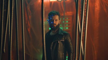 LED ışıkları olan bir kulaklık takan genç adam siyah asma çubukların arkasında durup kameraya bakıyor. Siberpunk ve fütüristik kavram. Arka planda neon ışıkları.