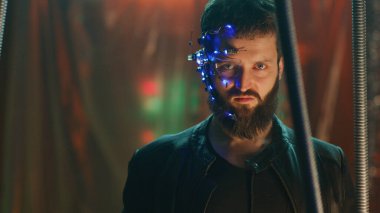 LED ışıkları olan bir kulaklık takan genç adam siyah asma çubukların arkasında durup kameraya bakıyor. Siberpunk ve fütüristik kavram. Arka planda neon ışıkları.