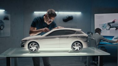 Kıdemli otomotiv mühendisleri yüksek teknoloji otomobil imalat şirketinde çalışıyorlar. Biri prototip arabanın heykeli üzerinde çalışırken, diğeri de çizimler için dijital dokunmatik ekran tablosu kullanıyor..