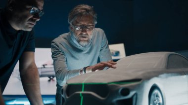 Kıdemli otomotiv mühendisleri, bir heykel prototip araba modelinin önünde mükemmellik için yeşil lazer ışığını kullanarak araba tasarımını tartışıyor. Yüksek teknoloji laboratuarında cam bir masaya yerleştirilmiş model bir araba..